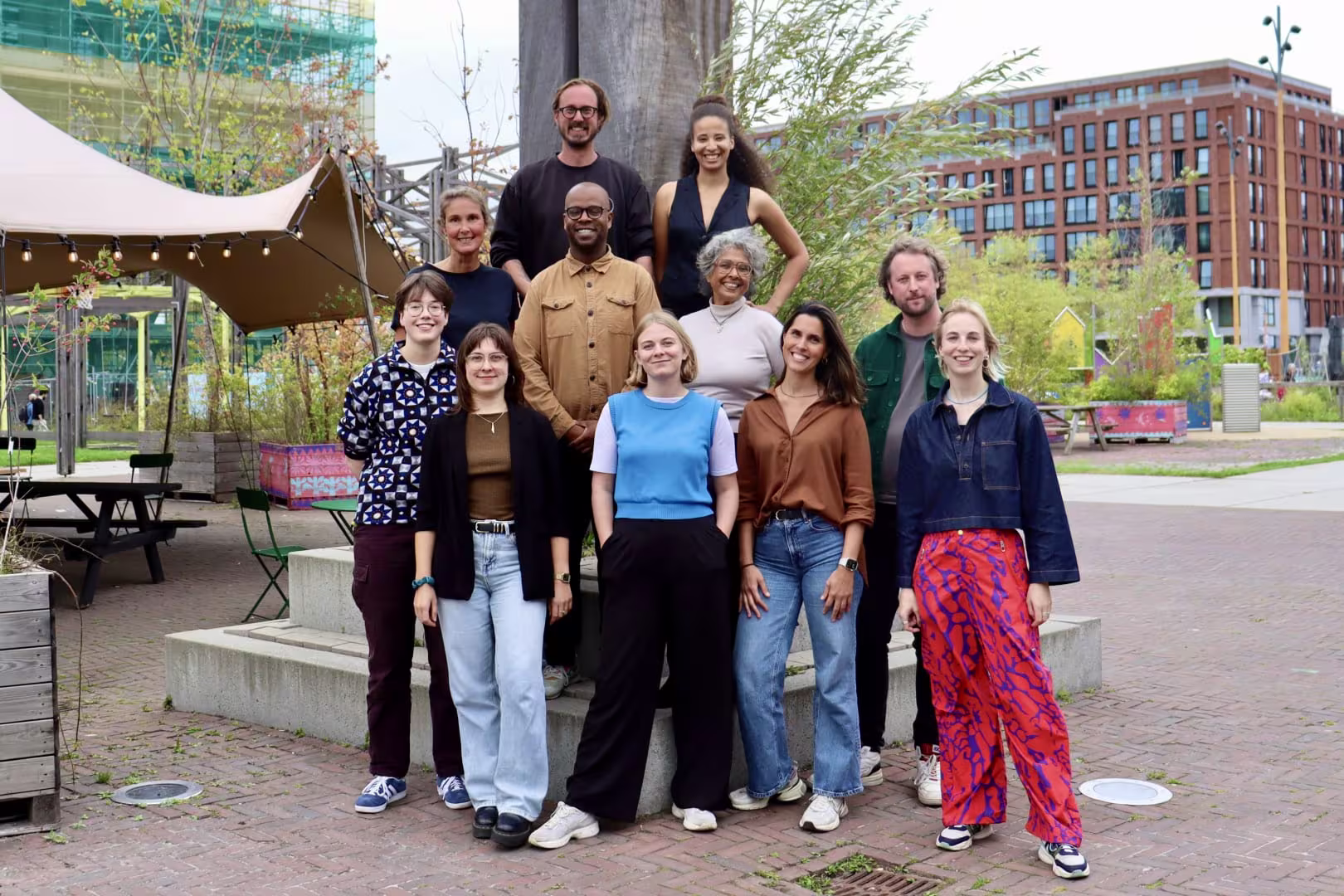 Group photo of a diverse team of eleven people outdoors in an urban setting, posing in front of a tree.