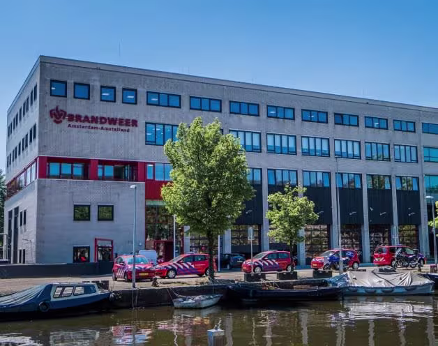 Hoofdkantoor van Brandweer Amsterdam-Amstelland aan het water, met brandweervoertuigen geparkeerd voor de deur.