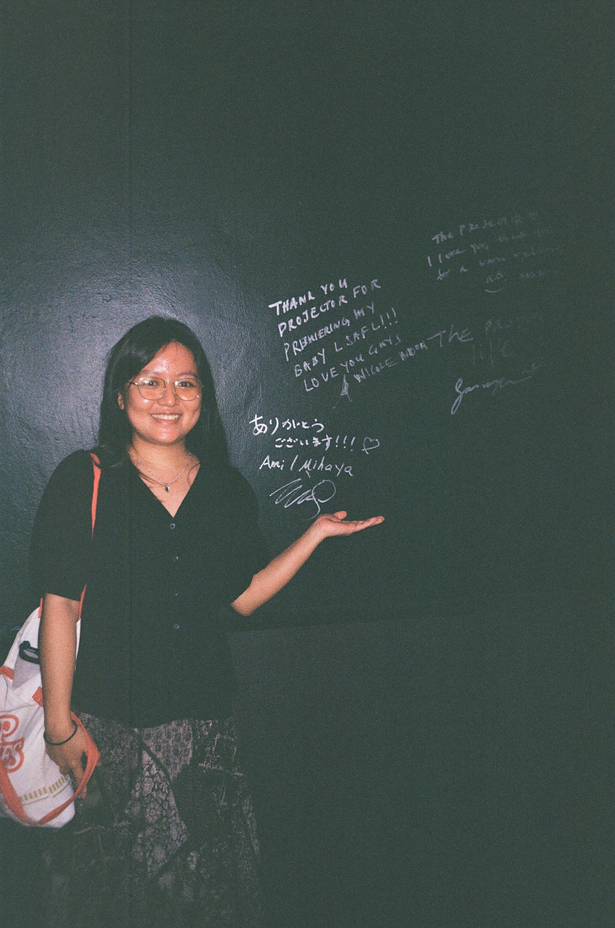 Photo of a person with long hair smiling next to a wall of autographs