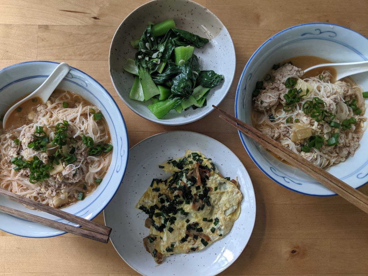 Table with three dishes: rice vermicelli in soup, oyster mushroom omelette with chives, stir-fried bok choy