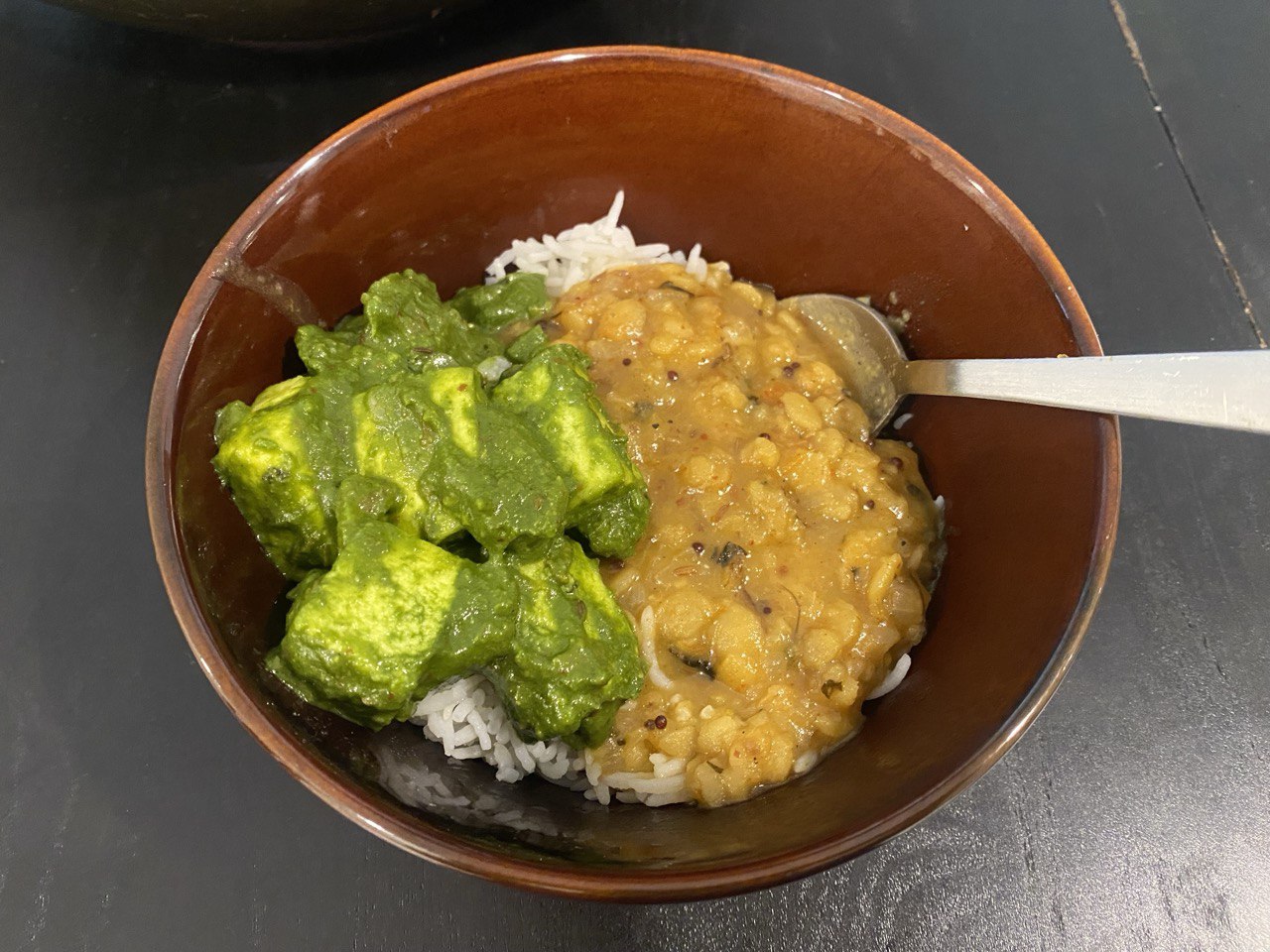 A bowl of basmati rice topped with mushroom palak paneer and daal