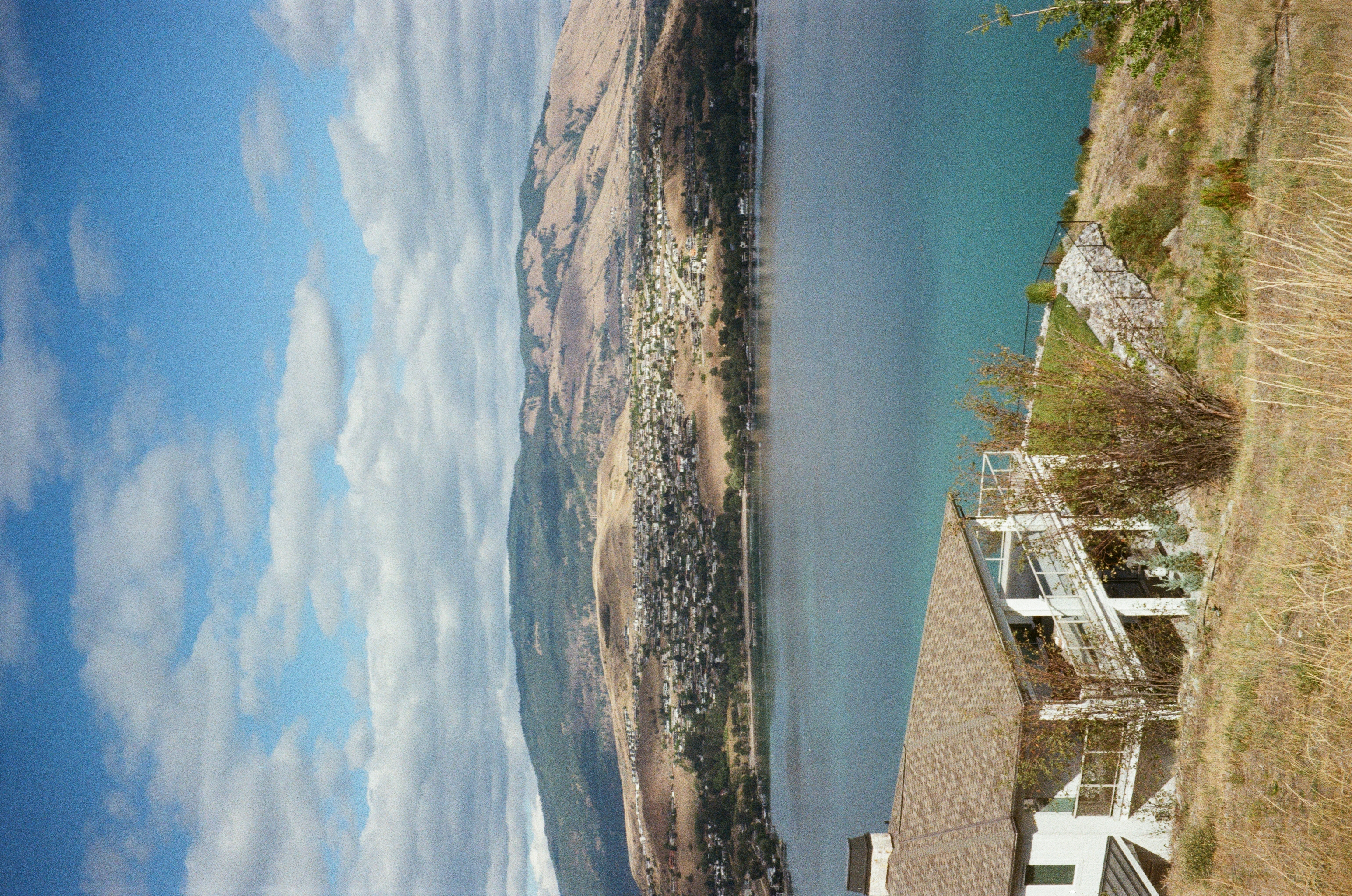 Kelowna, British Columbia. The photo is shot on a hill that overlooks the water. The hills appear dry and arid. The water is turquoise.