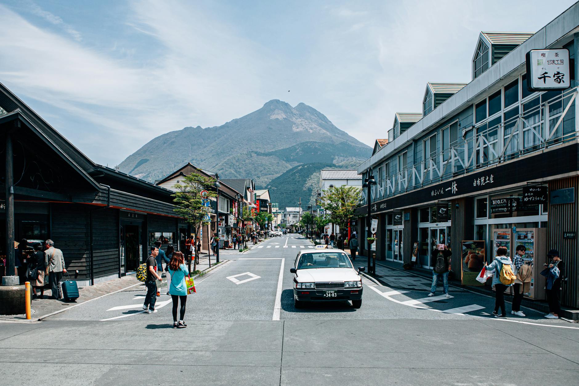 Dynamic town street scene with shopping and mountain backdrop, showcasing urban life.