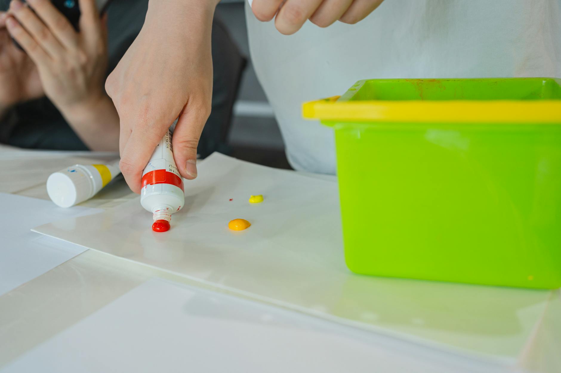 Hands squeezing colorful paint onto a sheet in a vibrant art class setting.
