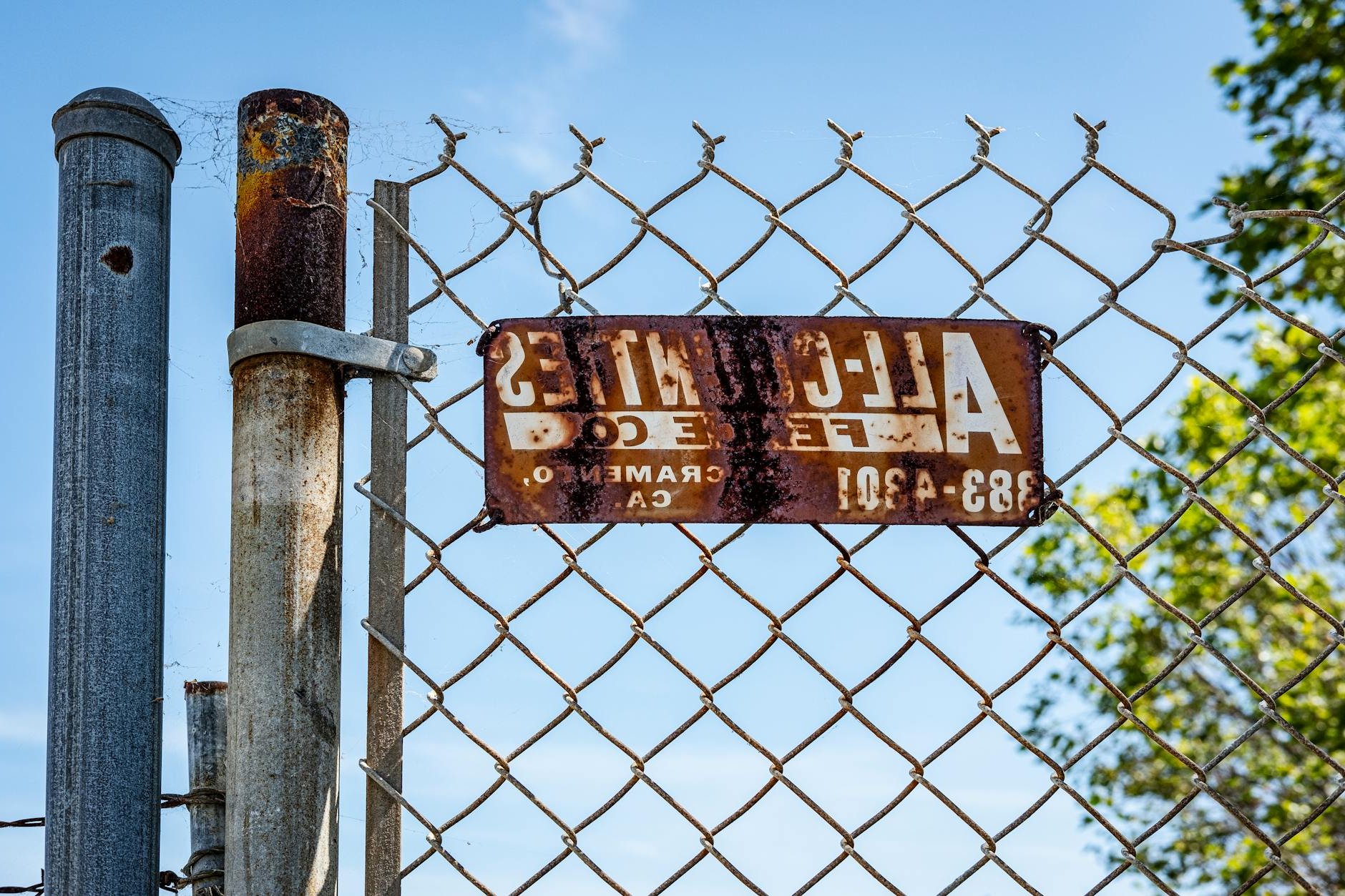 Close-up of a rusty chain link fence with a vintage sign, outdoors in daylight.