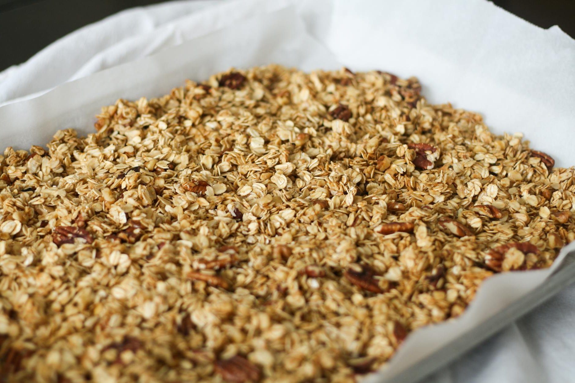 Freshly baked homemade granola with oats and pecans on parchment paper.