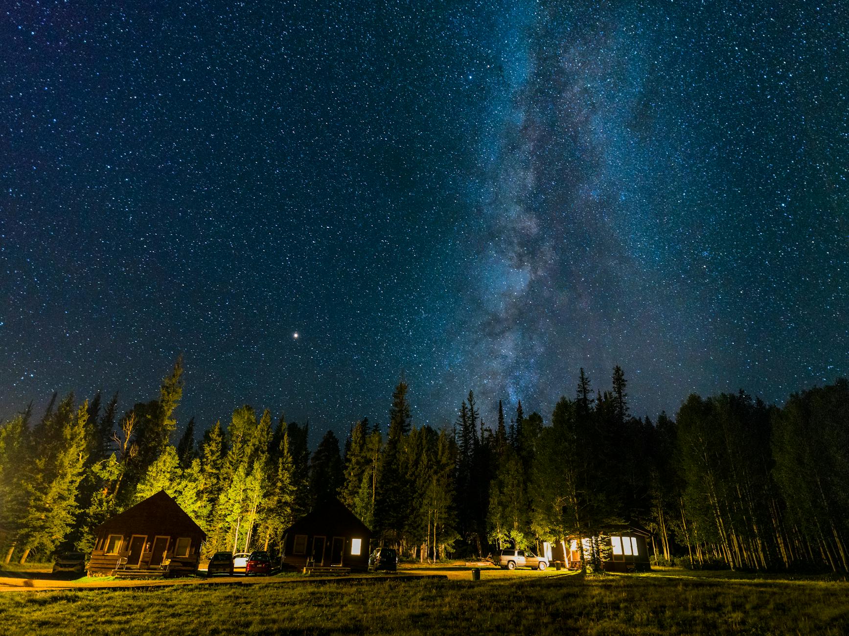 A breathtaking view of the Milky Way galaxy over cabins and forest at night in a starry sky.