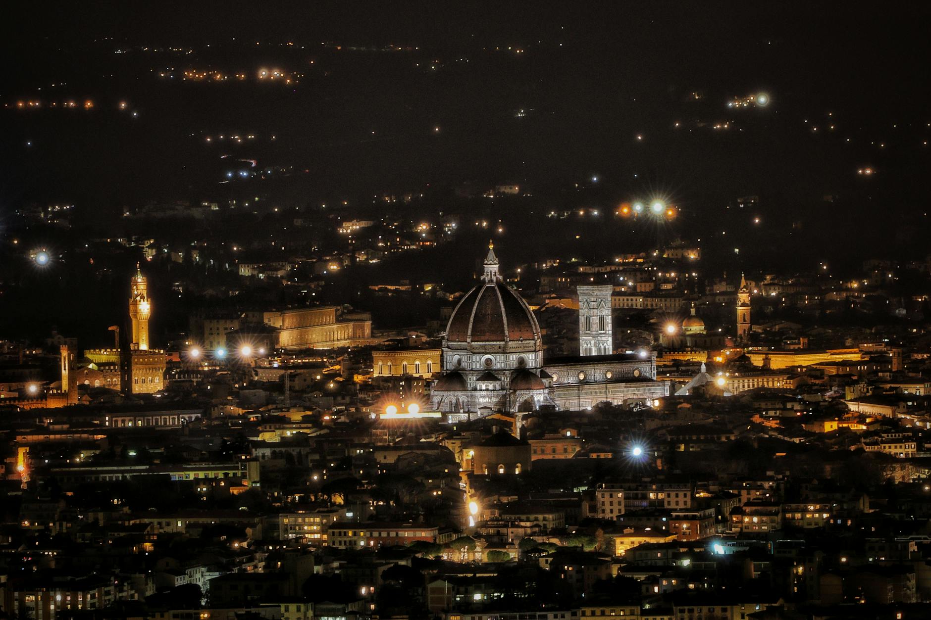 Nighttime view of the illuminated Florence Cathedral with surrounding cityscape.