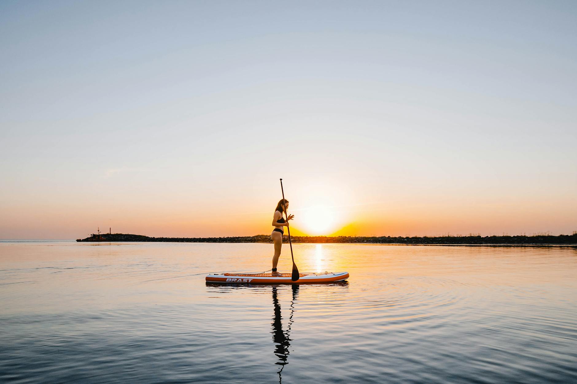 Woman paddleboarding on calm waters at sunset in Kuiviži, Latvia.