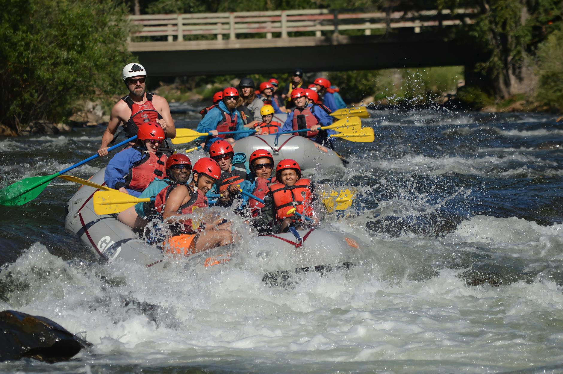 Group of people whitewater rafting with paddle splashes on a river, wearing safety gear.