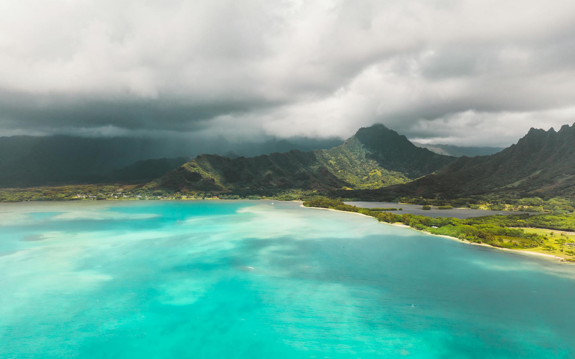 Breathtaking aerial shot of Oahu's turquoise waters and lush mountains under cloudy skies.