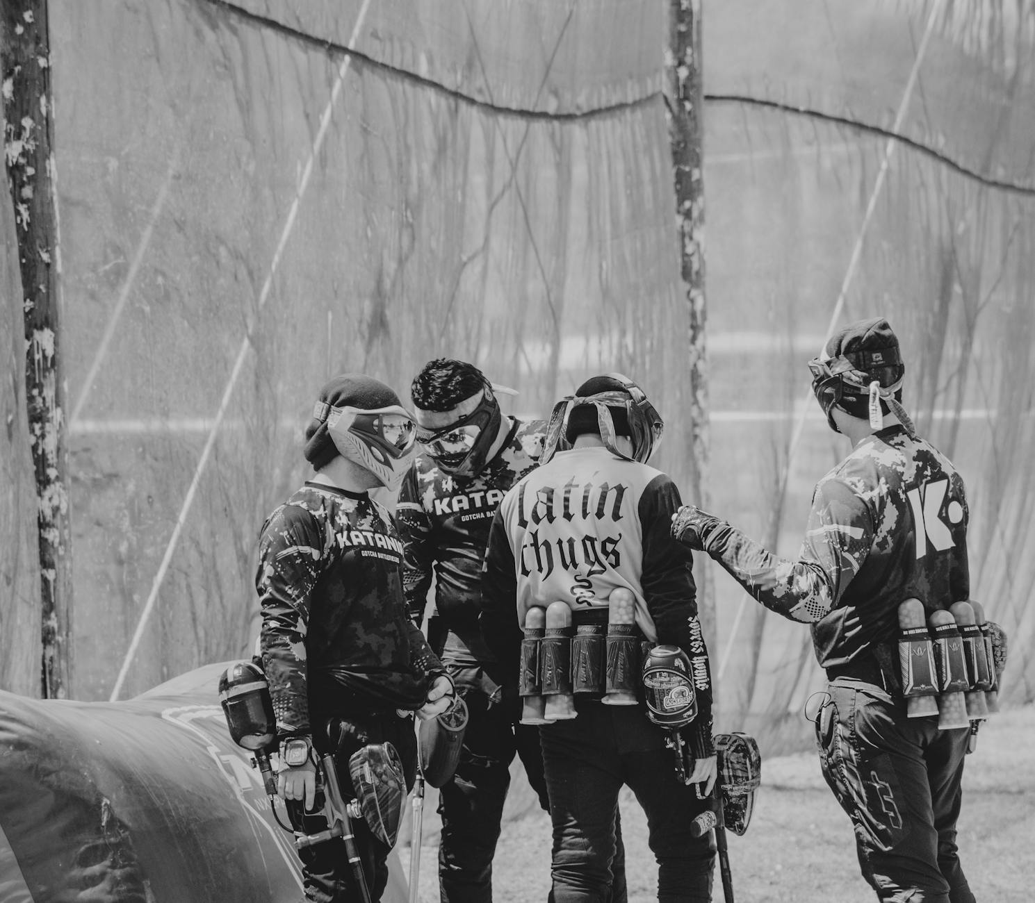 Black and white photo of a paintball team discussing strategy during a game outdoors.