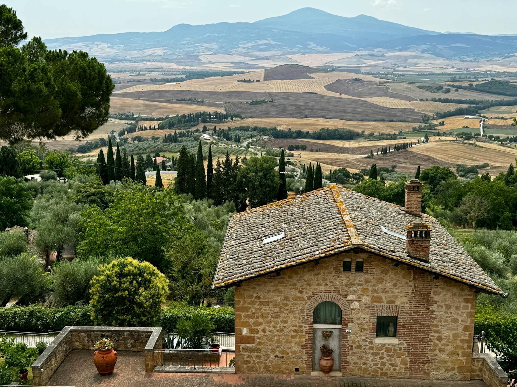 Scenic view of a rustic house in Val d'Orcia, Tuscany, Italy with rolling hills and lush greenery.