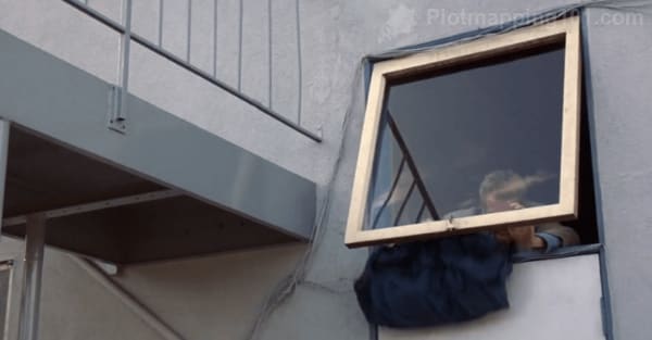 Leonard lifts a large square window pane to sneak out of the back of the tattoo parlor.