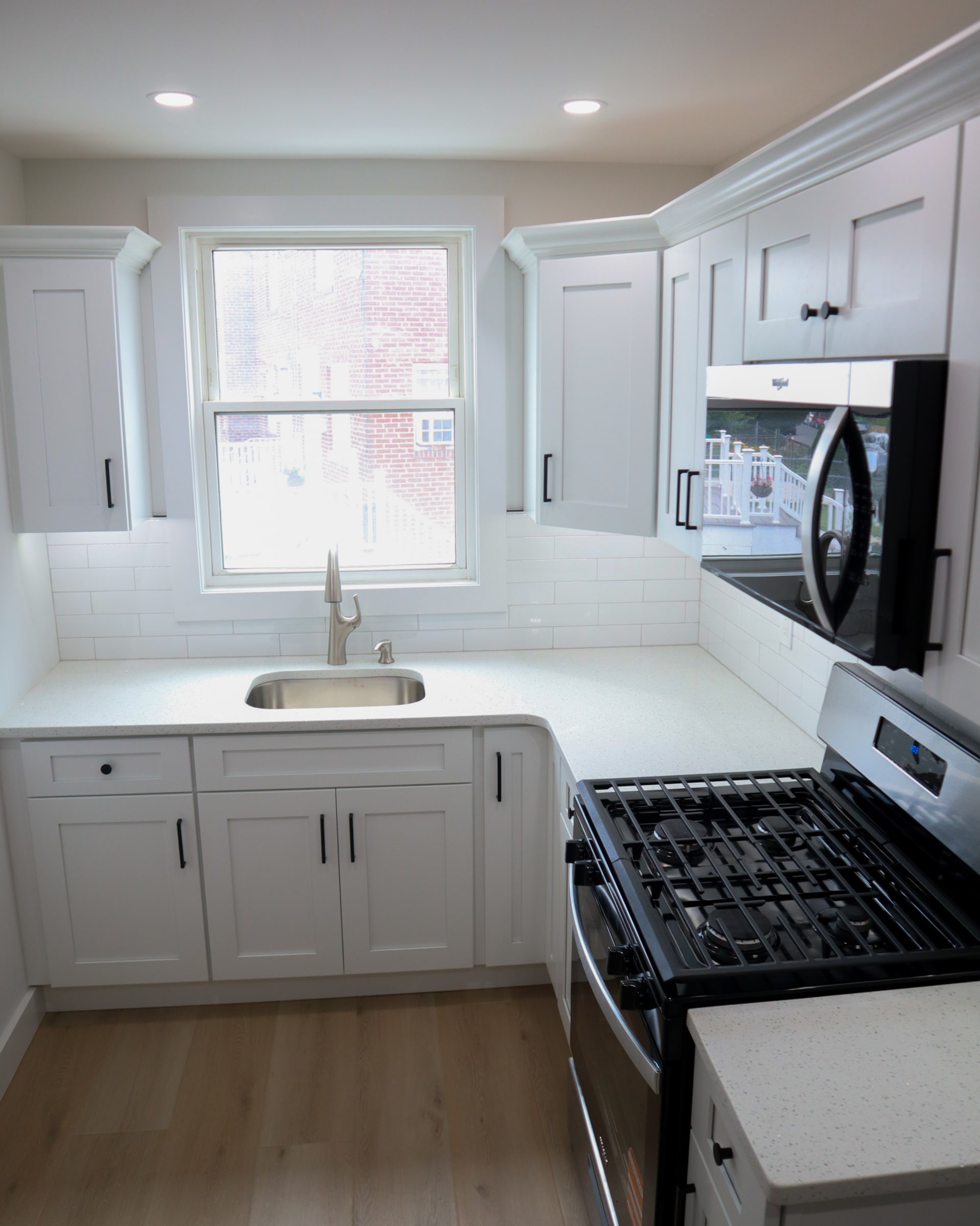 Finished L-shaped kitchen remodel with white shaker cabinets and stainless appliances