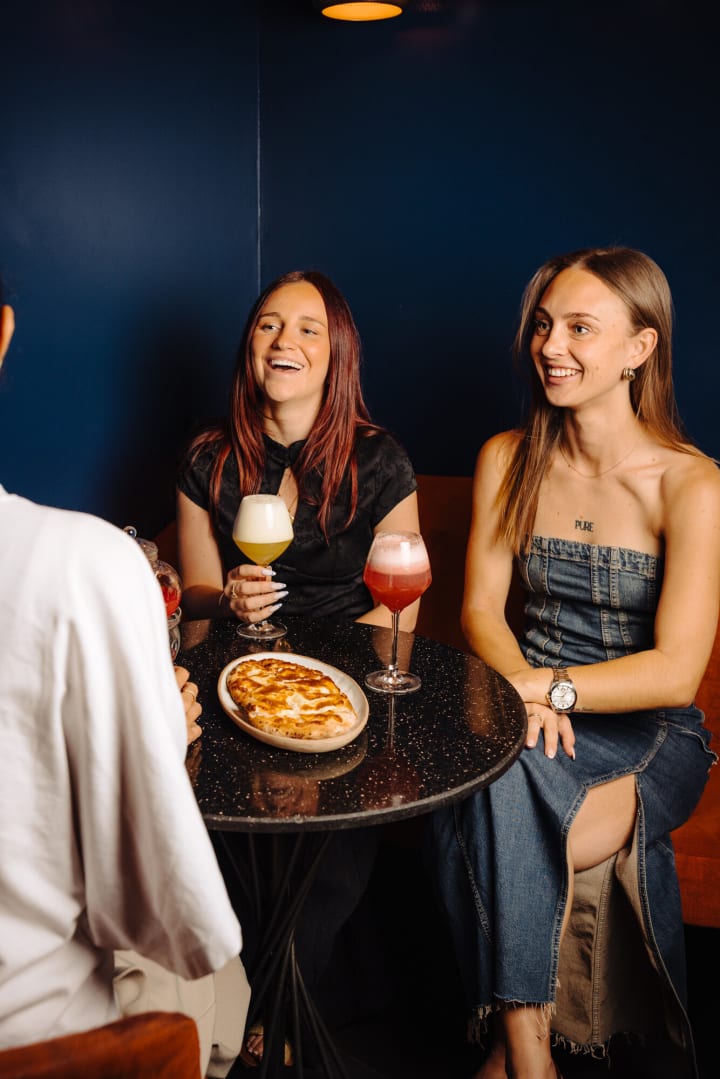 Deux amies qui rient autour d'une table, cocktails et pizza