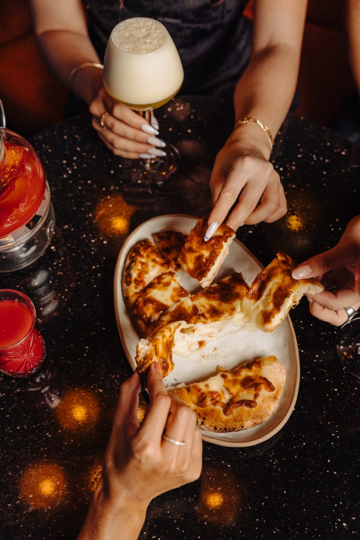 Des mains qui partagent une pizza fondante sur le marbre noir