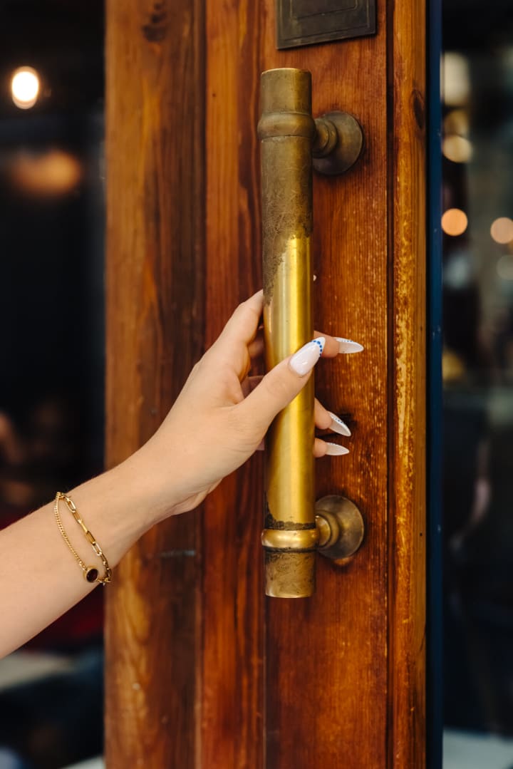 Une main sur la longue poignée en laiton de la porte du Pacific Lounge