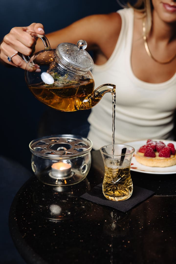 Thé servi depuis une théière en verre, tartelette aux framboises sur la table