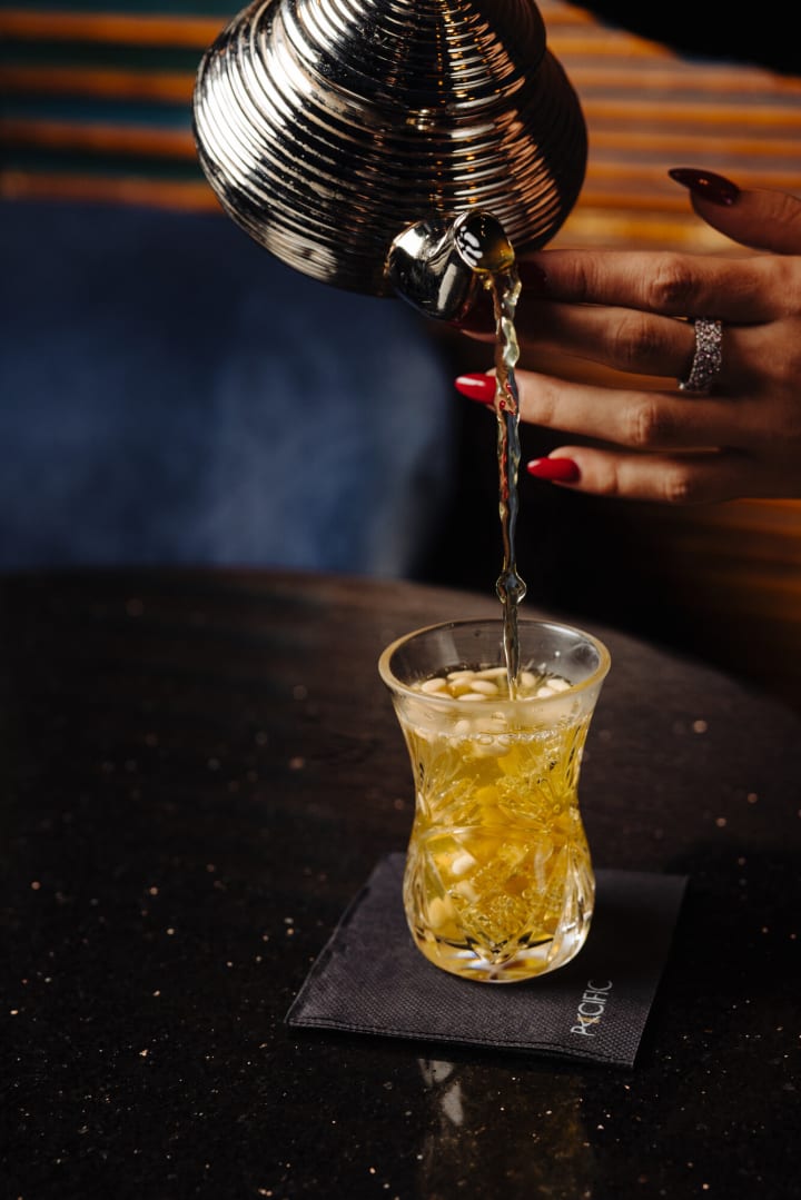 Thé versé depuis une théière argentée dans un verre ciselé