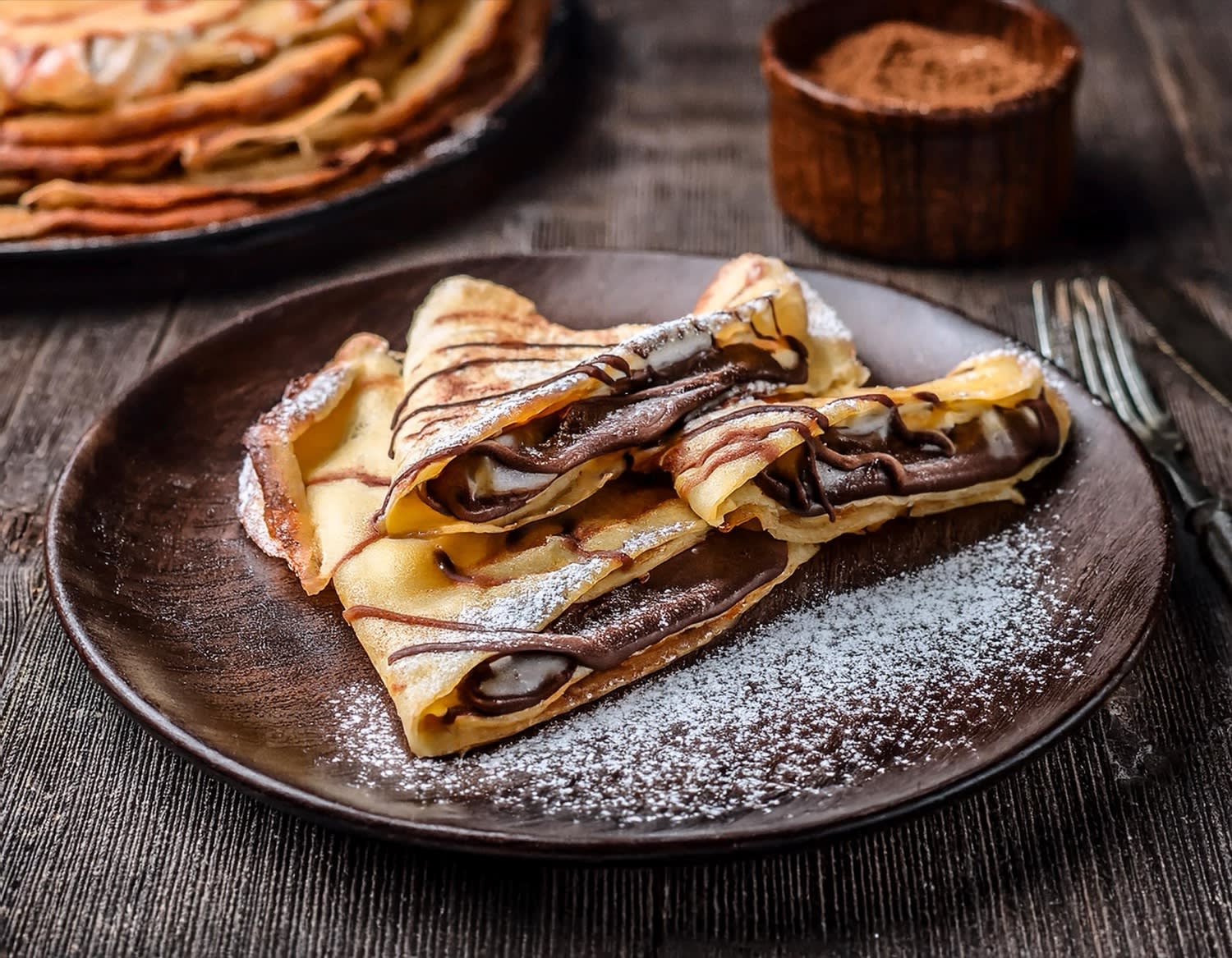 Crêpes au chocolat et sucre glace sur assiette rustique