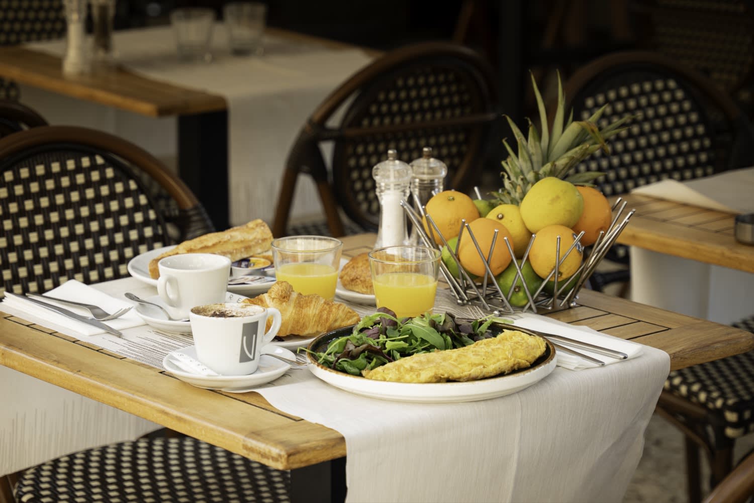 Petit-déjeuner dressé en terrasse, chaises en rotin