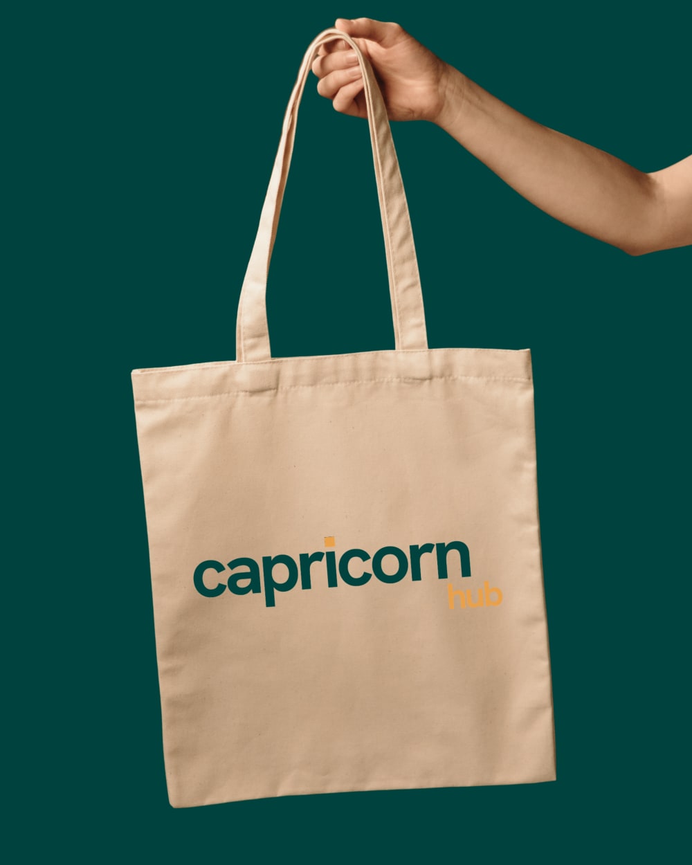 A cream Capricorn Hub tote bag held up against a deep green background