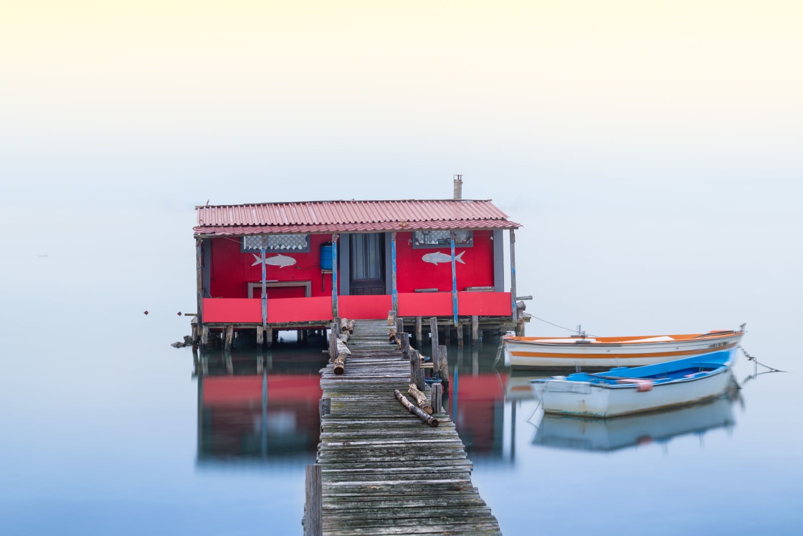 Red boathouse and boats on a tranquil lake at sunrise