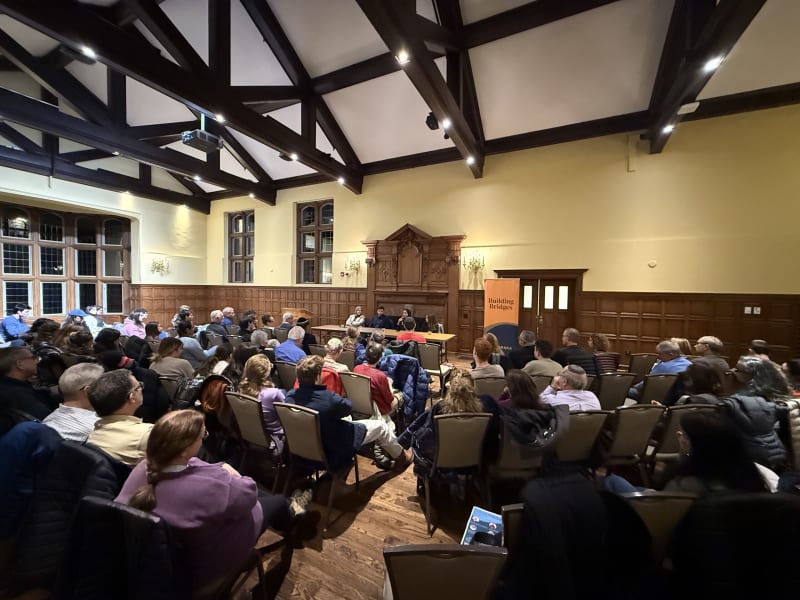 Speaking tour panel in a timber-beamed hall packed with listeners