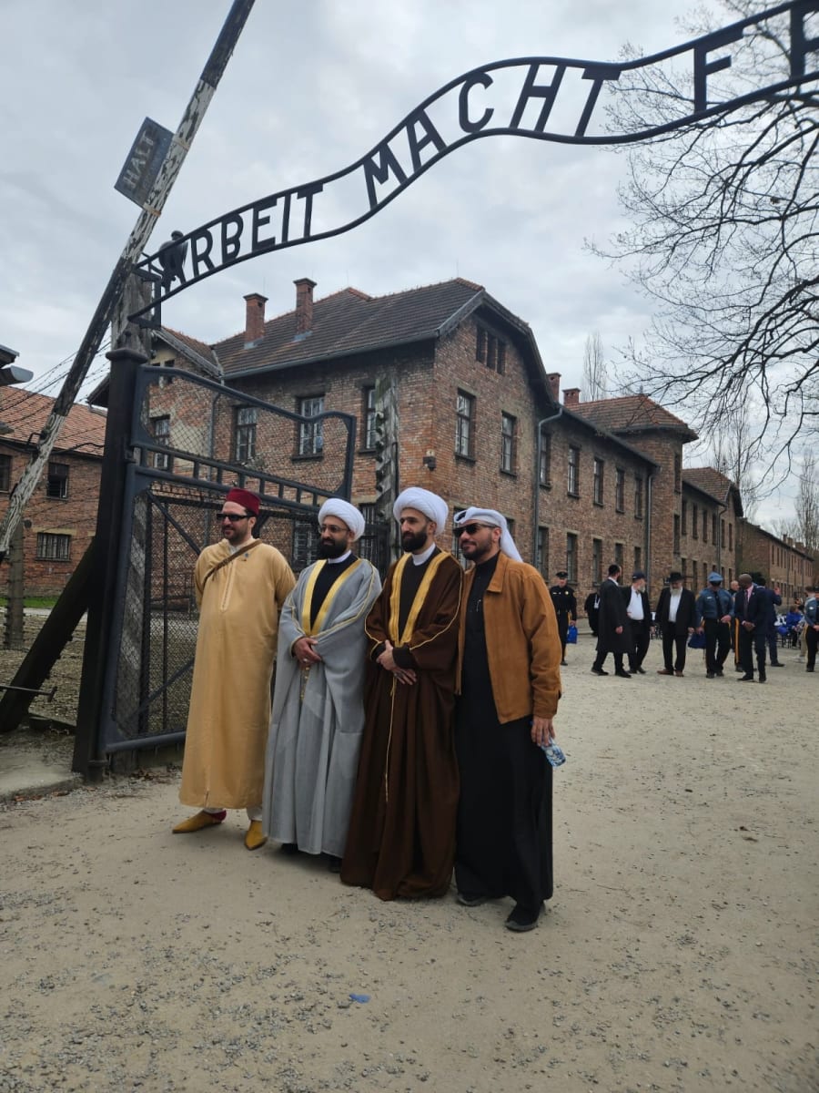 Imams in traditional dress at the Arbeit Macht Frei gate at Auschwitz