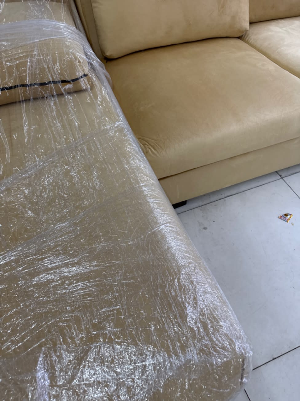 Corner junction of new beige L-shape sectional sofa with plastic protective wrapping still on chaise section, Bufaisal Ajman