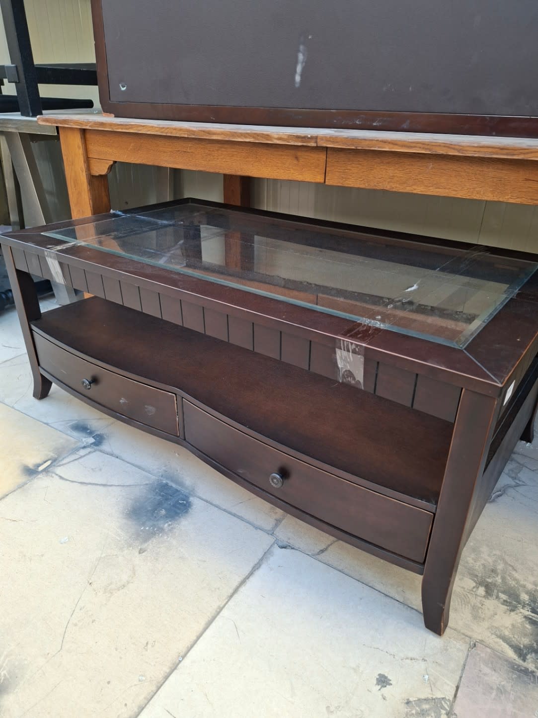 Side-angle view of used dark brown glass-top coffee table with lower shelf and 2 drawers at Bufaisal Ajman