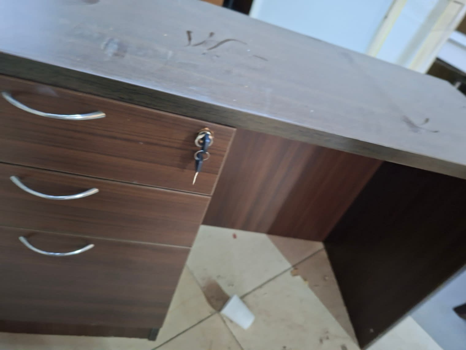 Close-up of used office desk top surface showing scuff marks and lockable drawer with key at Bufaisal Ajman