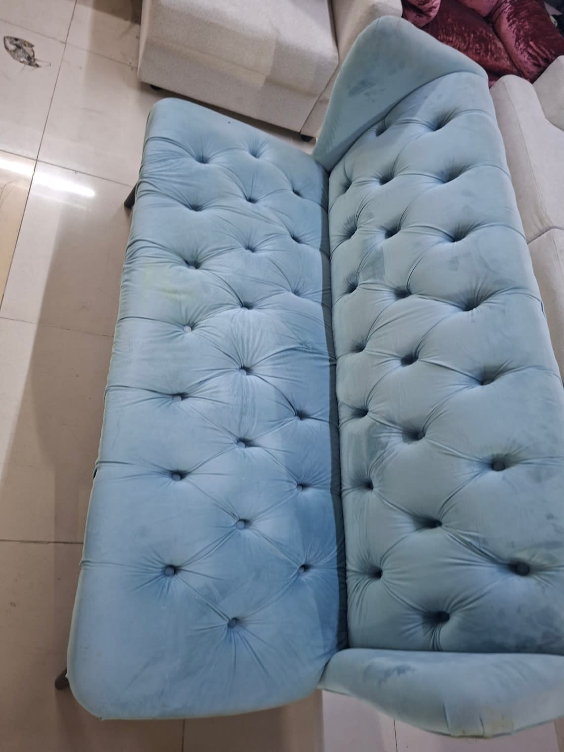 Top-down detail view of used light blue velvet Chesterfield sofa showing seat tufting and faint stain marks