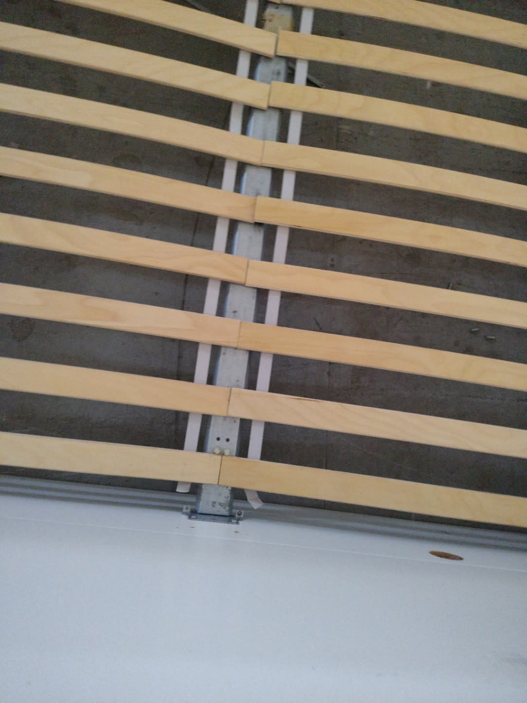 Close-up of wooden slats and centre metal support rail on used white queen bed frame