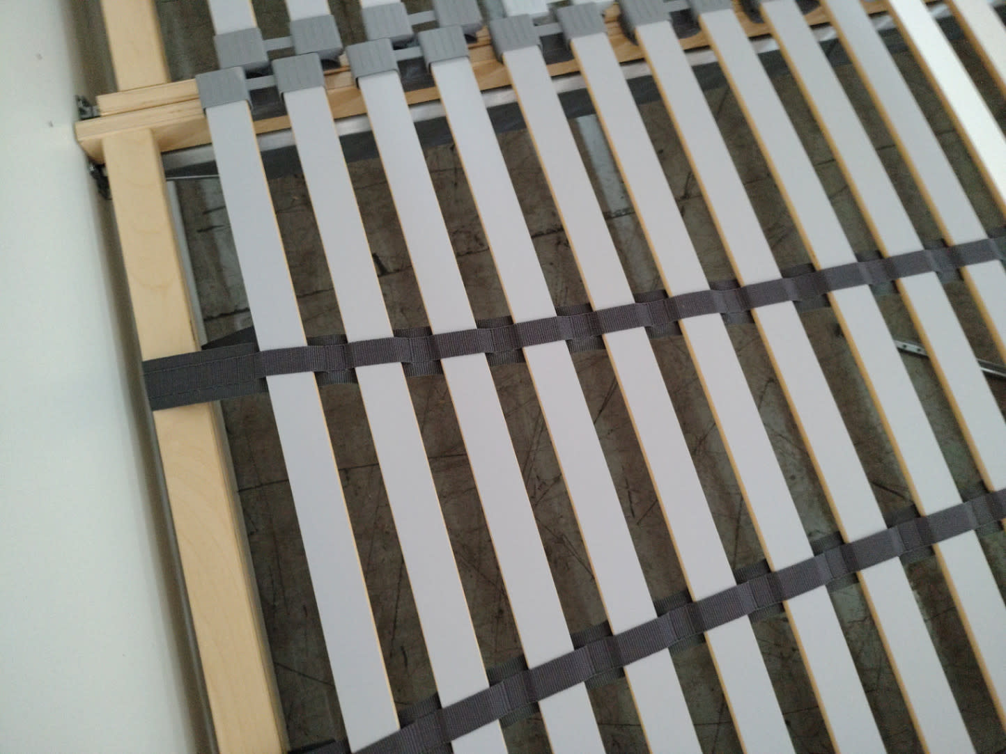 Close-up detail of sprung slat system with elastic strapping on used white queen bed frame