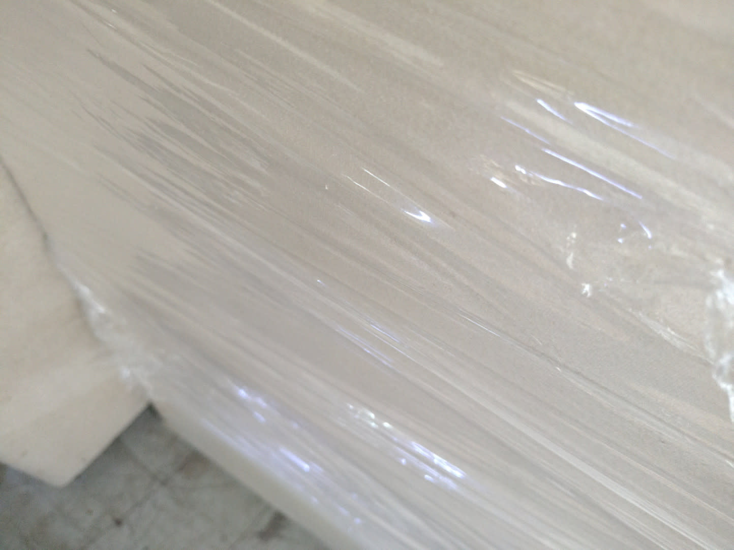 Close-up of cream fabric upholstered bed frame side panel wrapped in protective plastic at Bufaisal Ajman