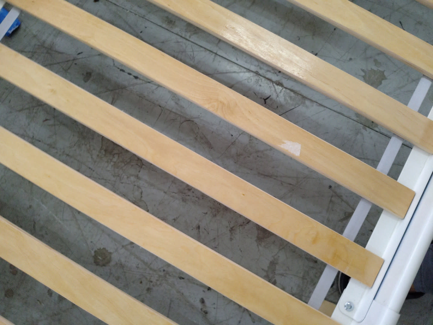 Close-up of wooden slats on used white single metal bed frame showing minor scuff on one slat