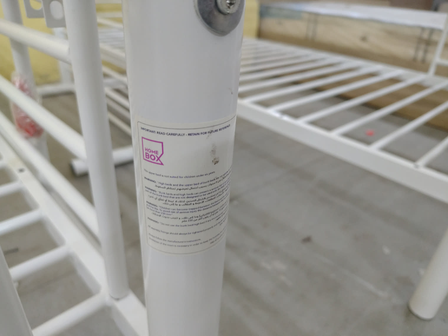 Home Box safety label on post of used white metal bunk bed frame at Bufaisal Ajman