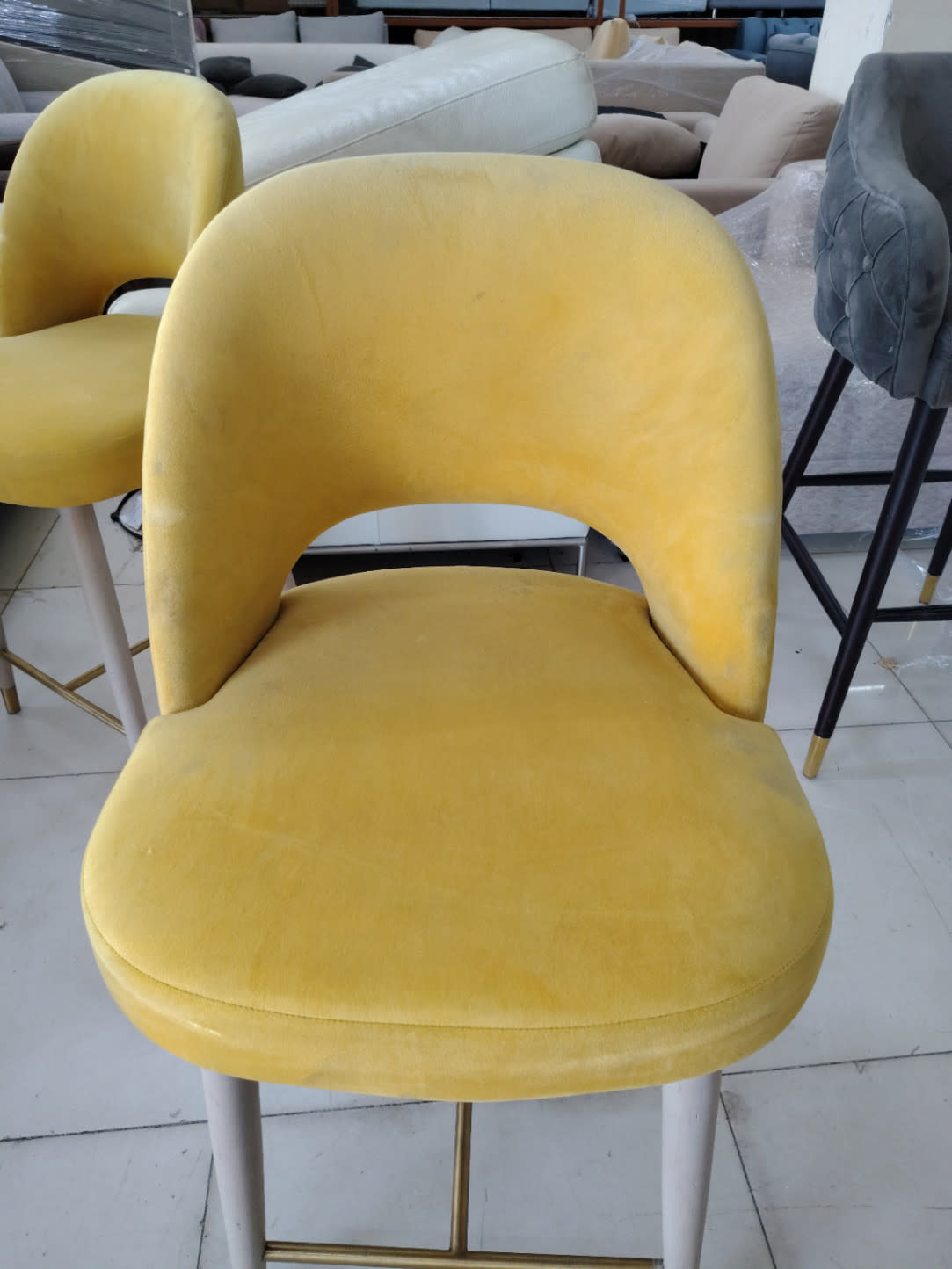 Close-up of used yellow velvet bar stool seat and backrest showing light surface wear