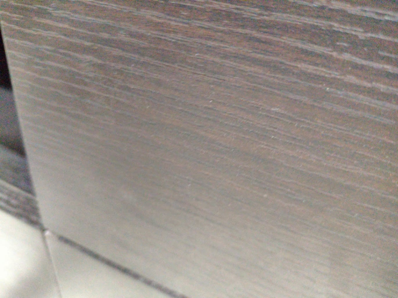 Close-up of wenge-finish side panel on used dark brown TV stand showing surface scratches