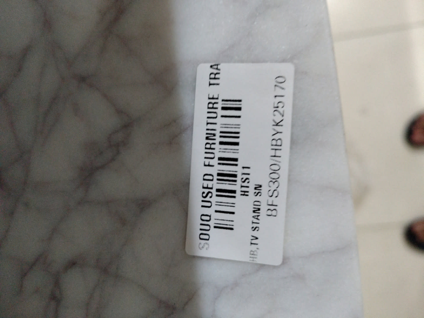 Bufaisal barcode label BFS300HBYK25170 on used TV stand marble-effect top surface at Shop C Ajman