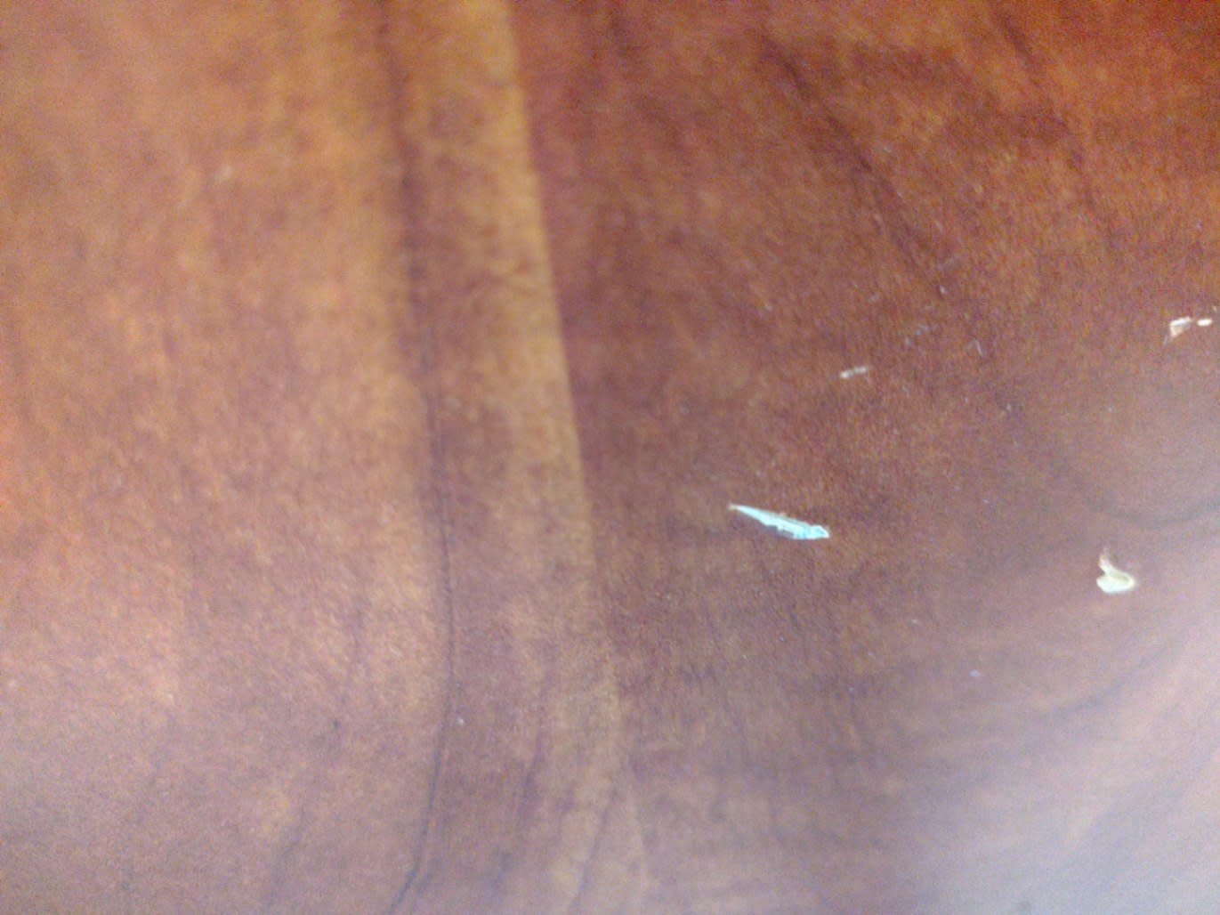 Close-up of brown laminate surface on used TV stand showing surface scratches