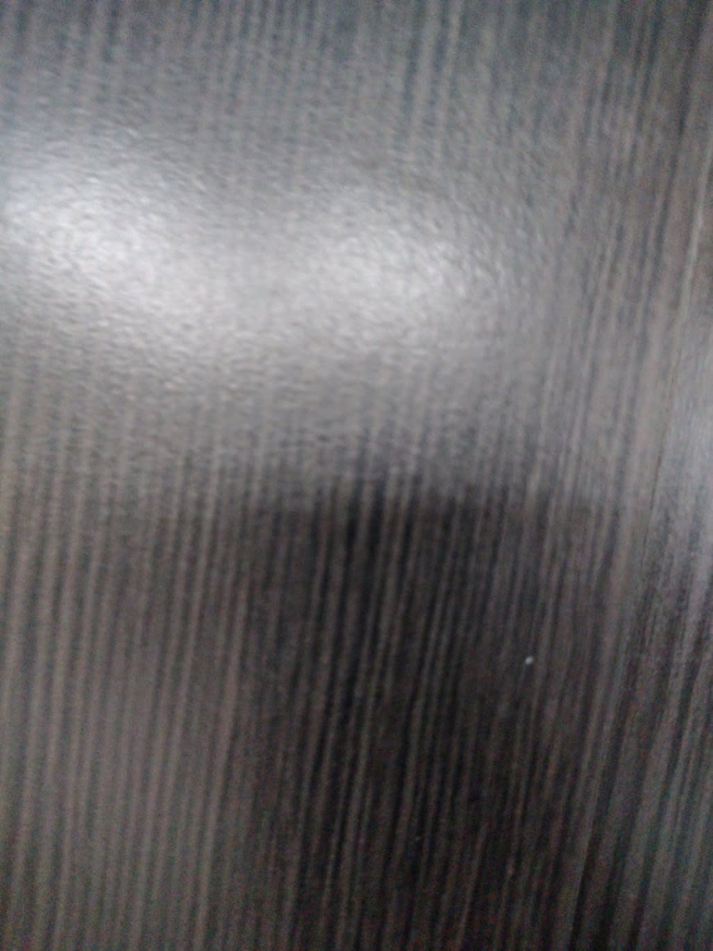 Close-up of dark wood-grain laminate surface on used TV stand showing minor surface scuff