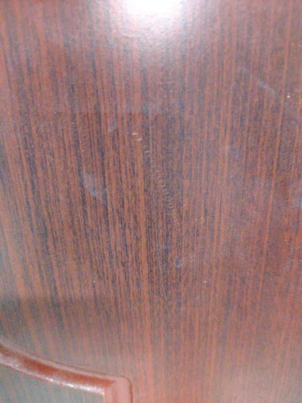 Close-up of side panel on used dark mahogany nightstand showing surface scuffs and scratch marks