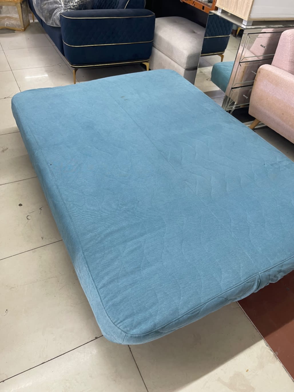 Used teal blue foldable sofa bed at angle showing quilted fabric surface and bed configuration