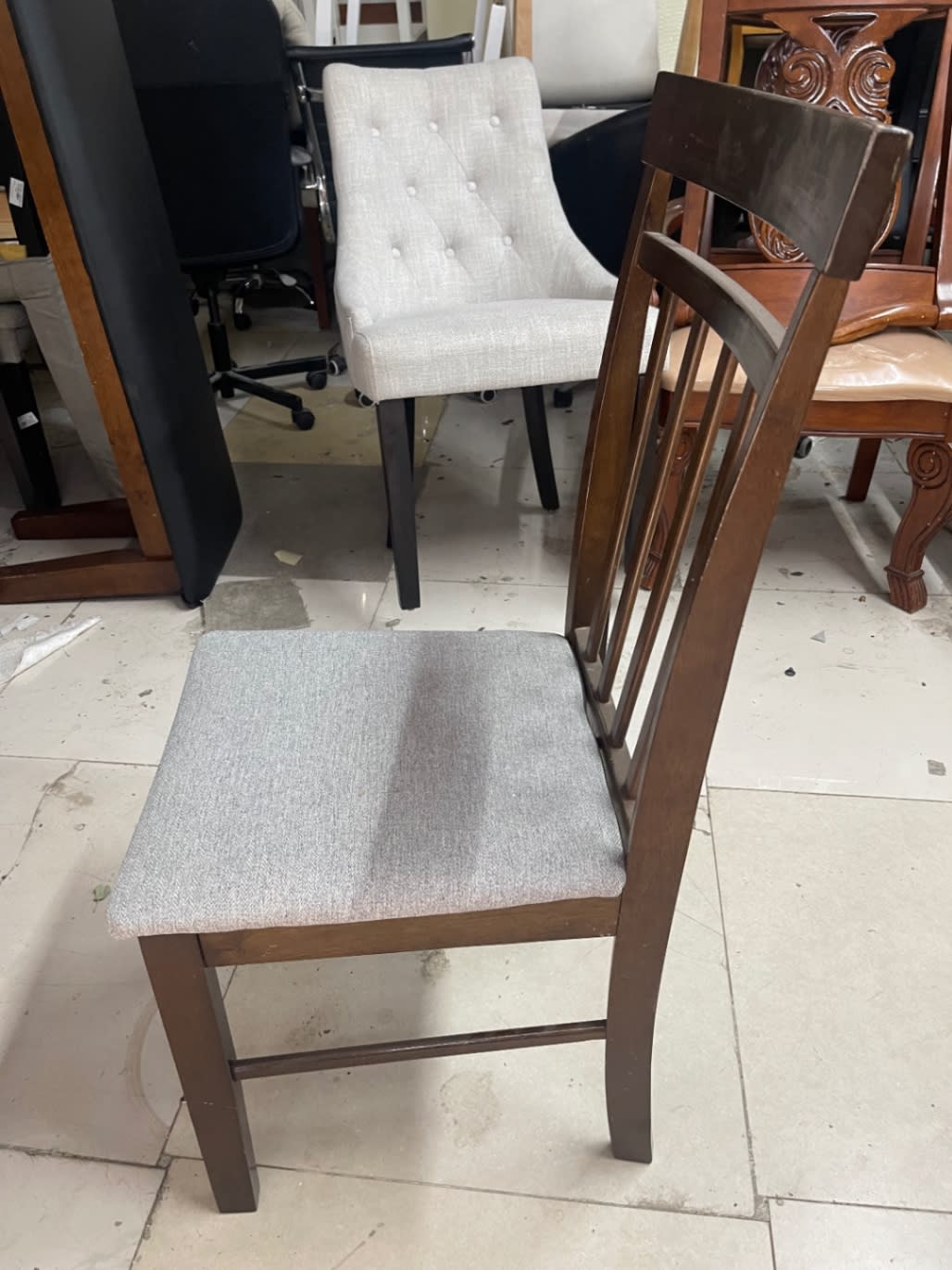 Rear angle of new dining chair showing dark wood frame structure and grey fabric seat at Bufaisal Ajman