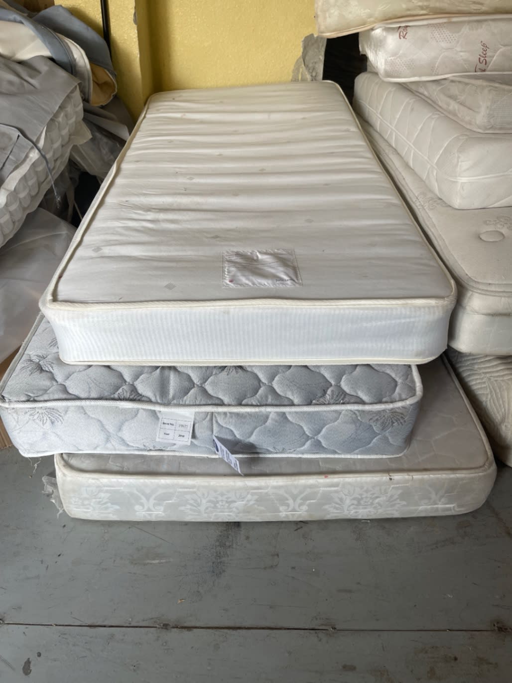 Used single mattresses stacked showing top surface and patch repair detail at Bufaisal Shop C Ajman