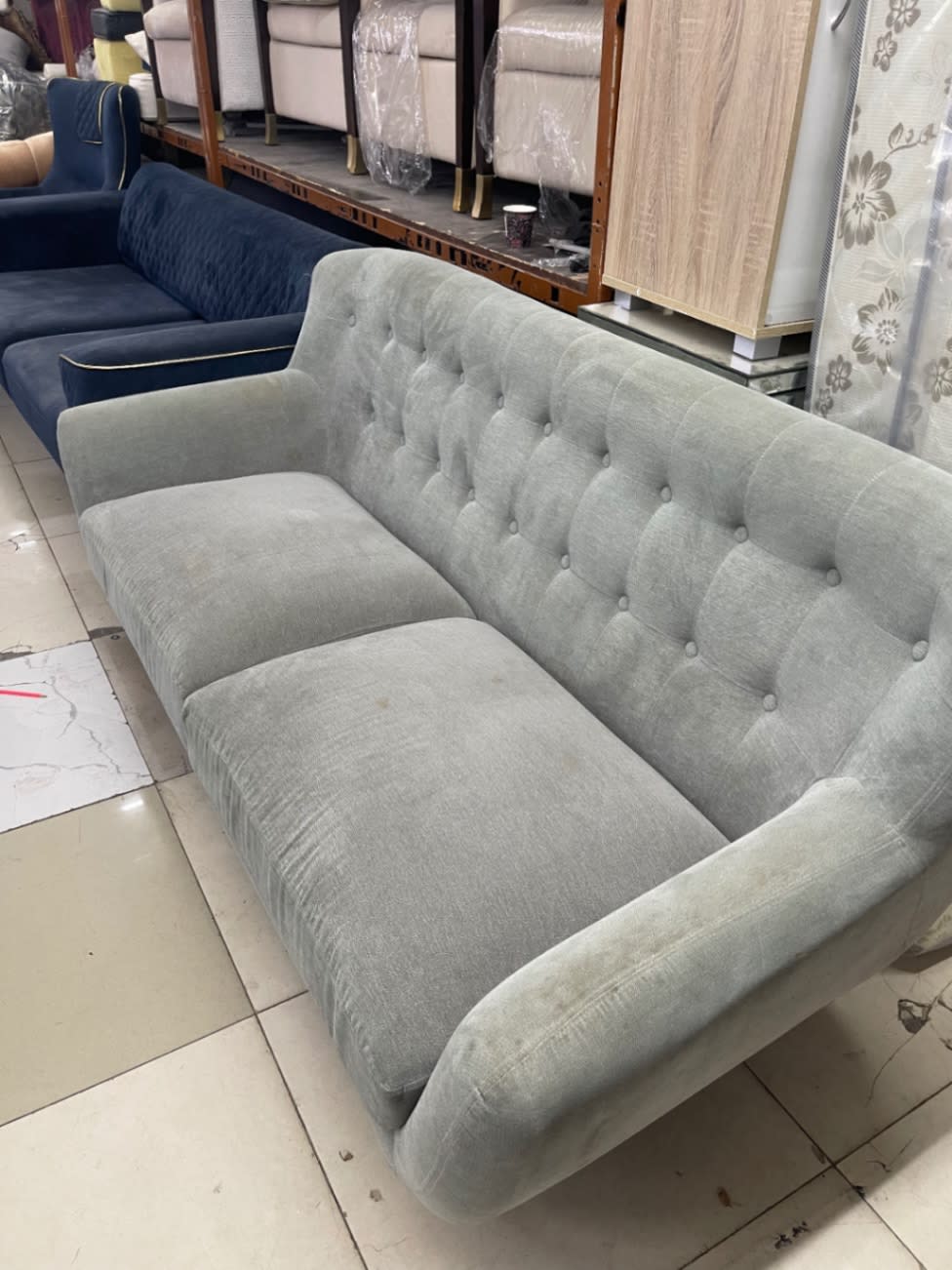 Side angle of used 3-seater tufted grey sofa showing button-tufted back at Bufaisal Ajman