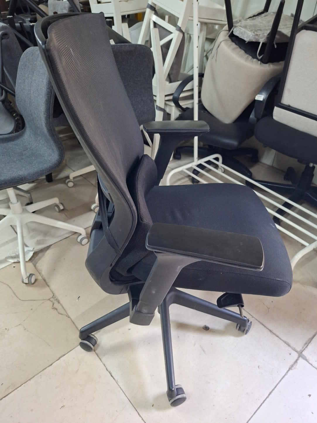 Side profile of used black high-back mesh office chair with adjustable armrests at Bufaisal Ajman